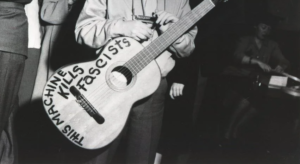 Woody Guthrie making political statement through rock & roll with a guitar with the words this guitar kills fascists written on it