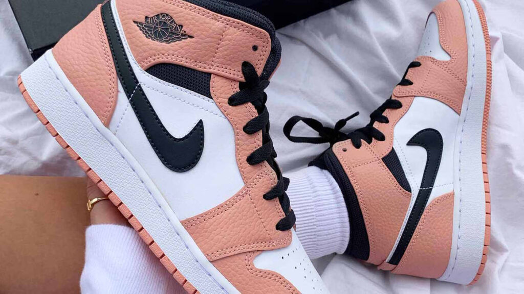 Picture of pink and white Nike air jordans, one on a foot the other being held